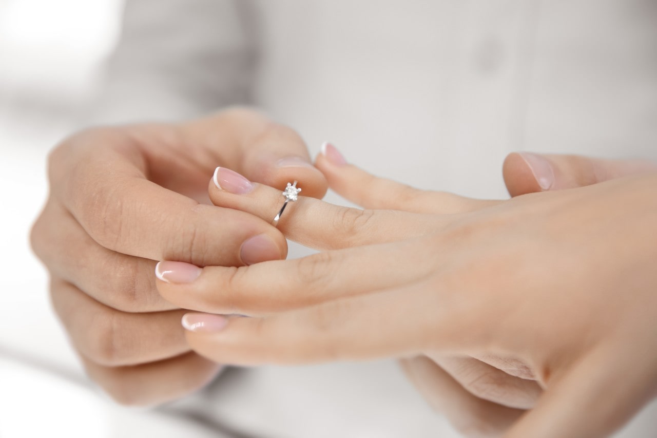 woman putting on round cut engagement ring