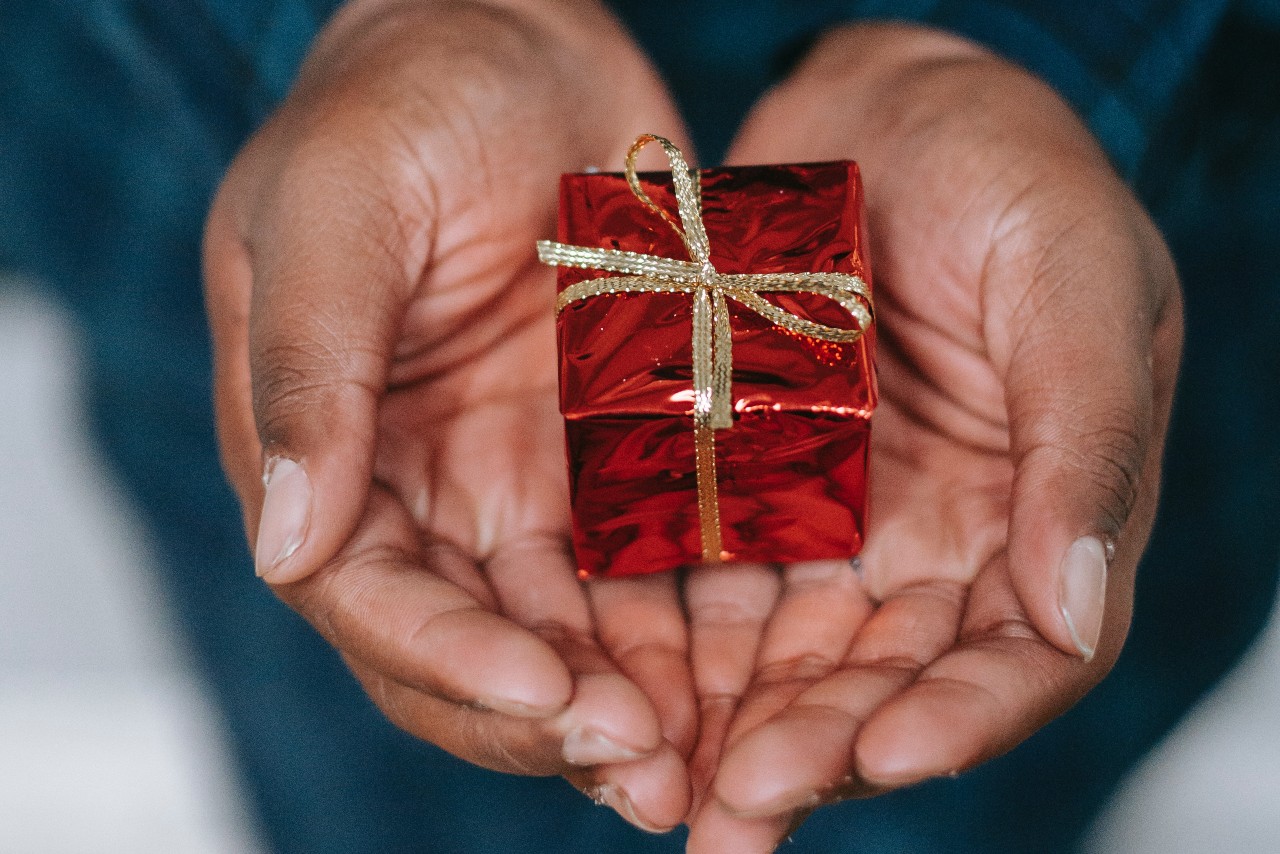 A close-up of a person’s hands, holding a tiny gift box decorated with gold ribbon.