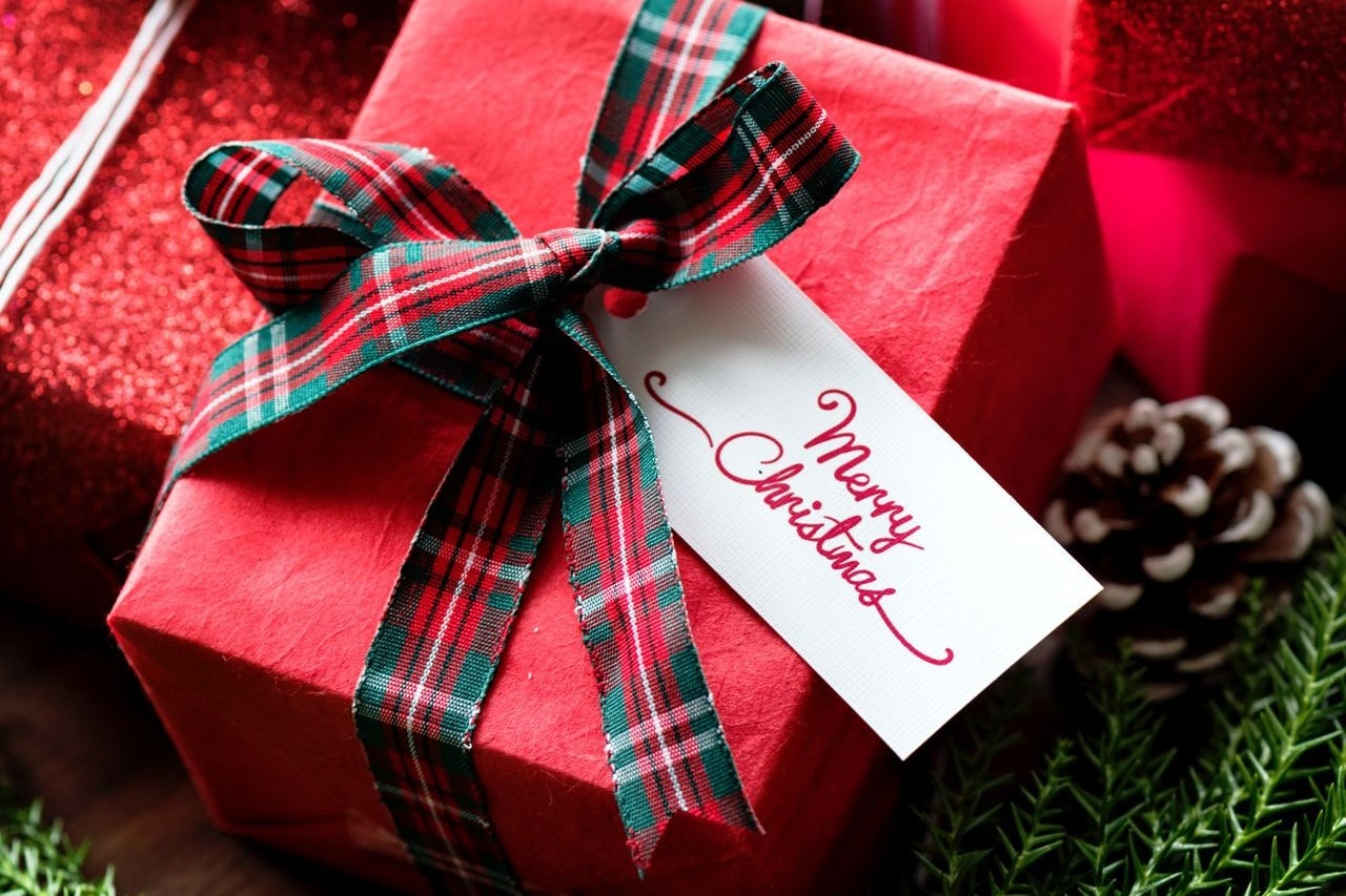 A close-up of a picturesque Christmas gift, wrapped with red paper and a plaid bow.