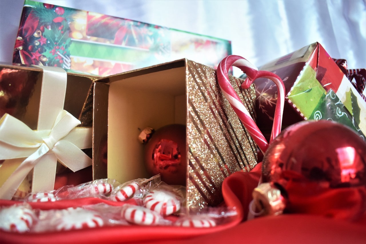 A close-up of a small pile of Christmas gifts among ornaments, candy canes and peppermints, with one open gift box on its side.