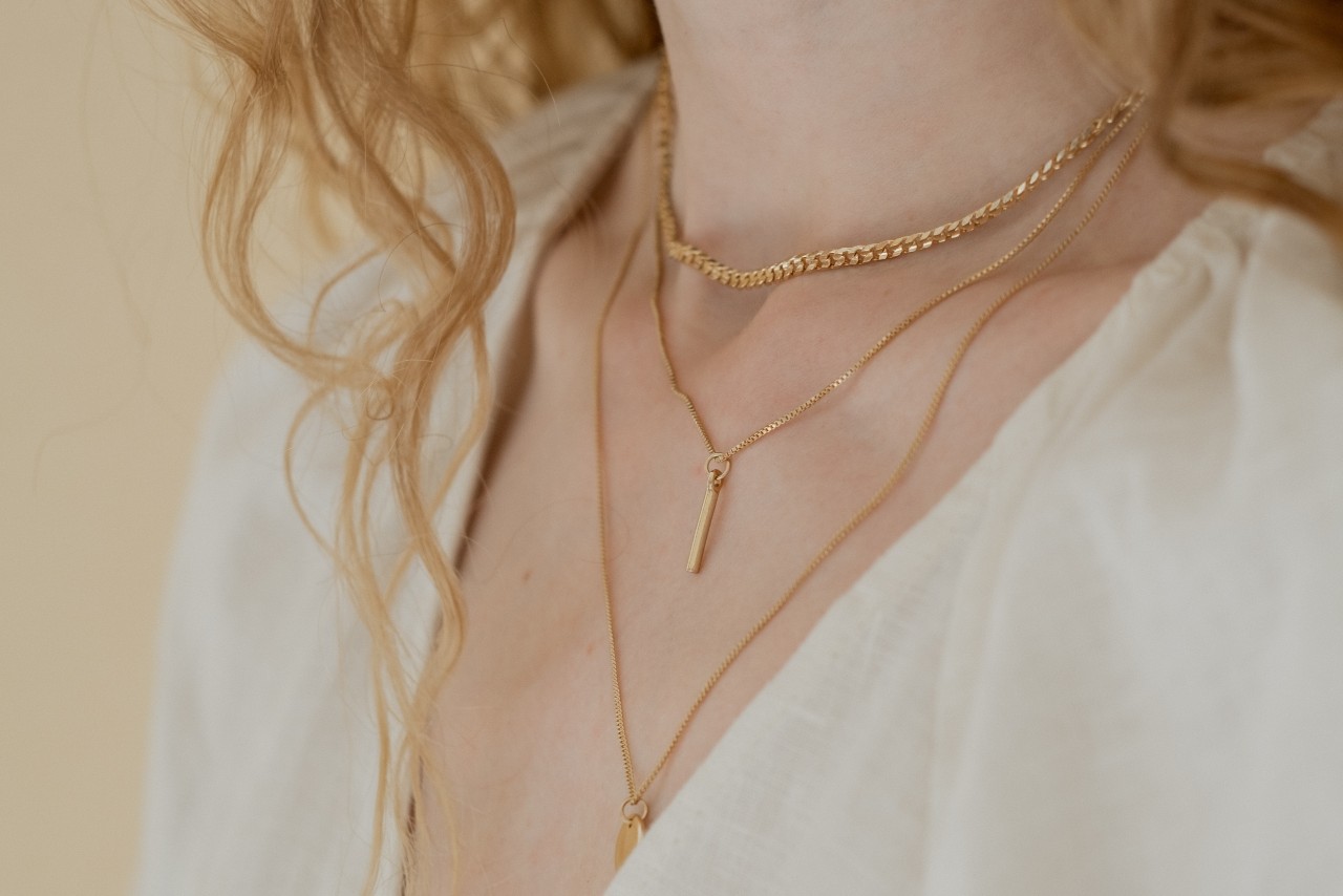 close up image of a woman’s neckline, adorned with three simple gold necklaces