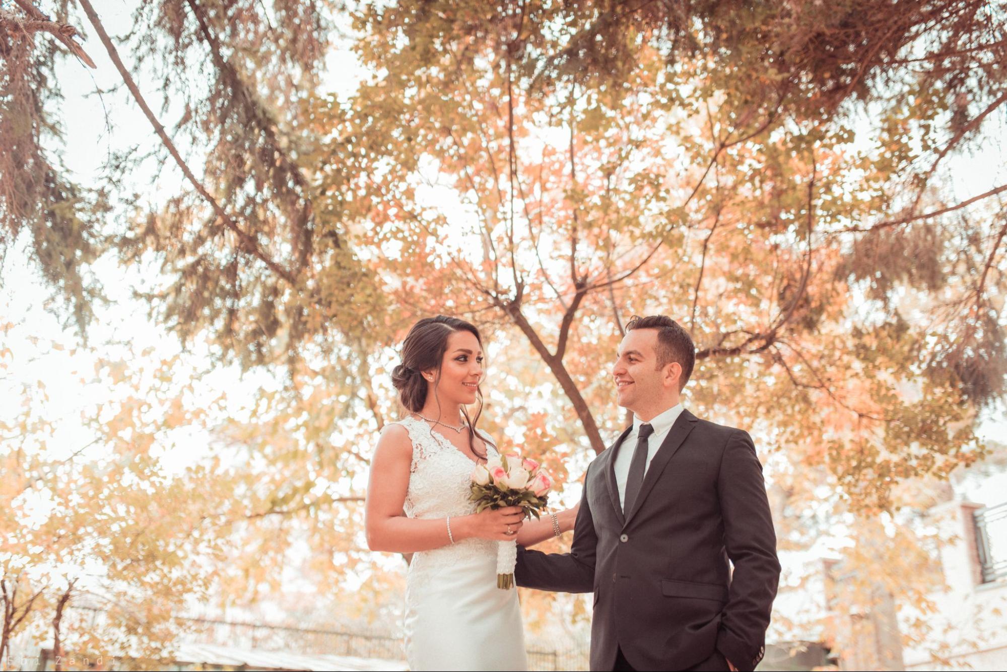 a bride and groom smiling at each other under fall trees on their wedding day