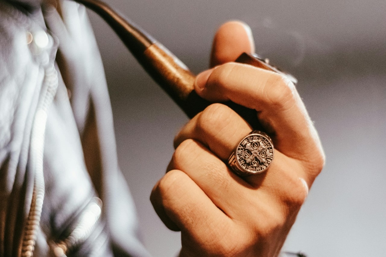 a man’s hand holding a pipe and wearing a signet ring