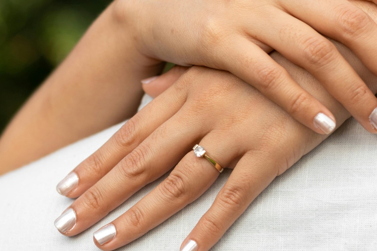 a woman’s hands resting on someone’s back, adorned with a solitaire engagement ring