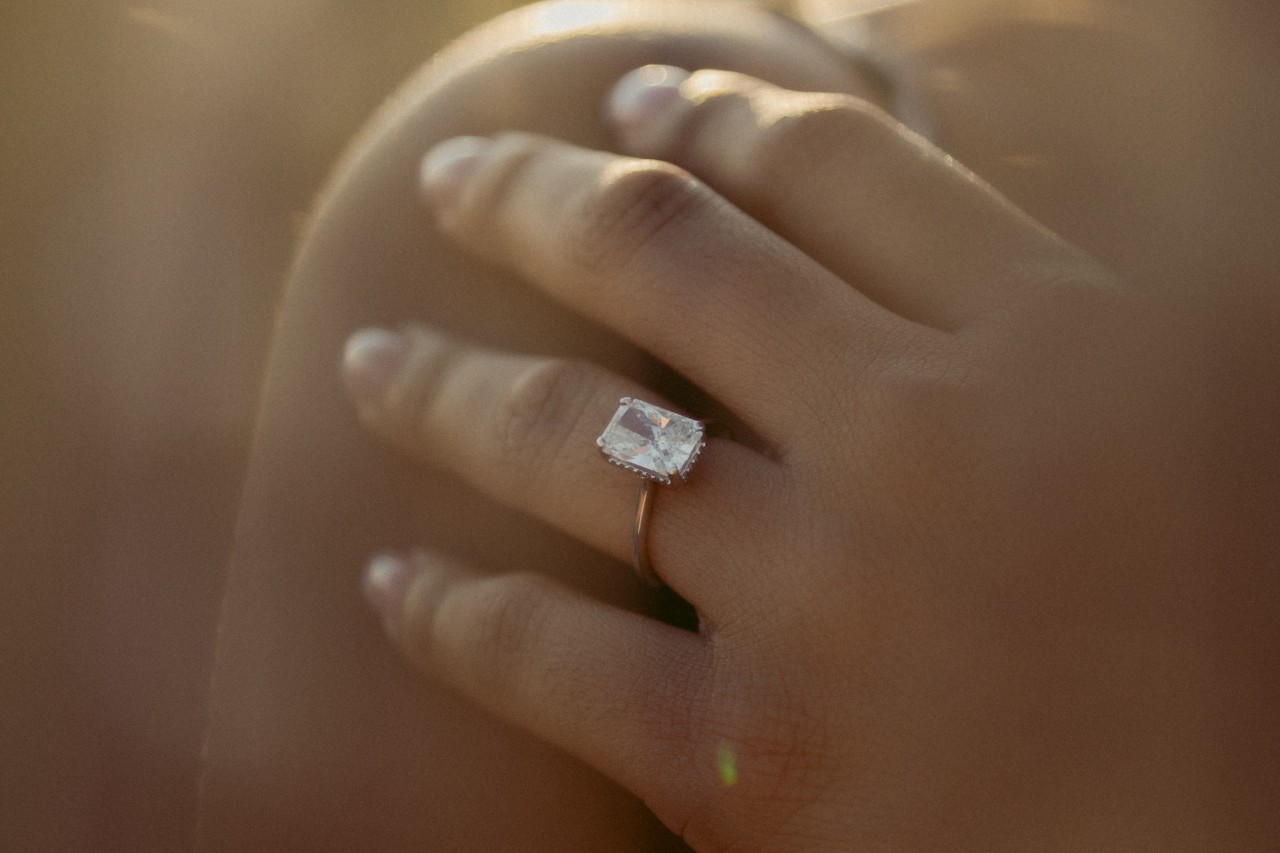 a woman’s hand resting on her shoulder, adorned with a solitaire emerald cut engagement ring