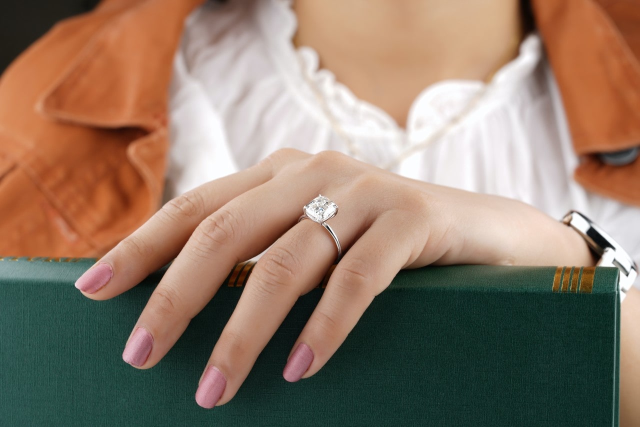 a woman’s hand resting on a green box, adorned with a cushion cut engagement ring