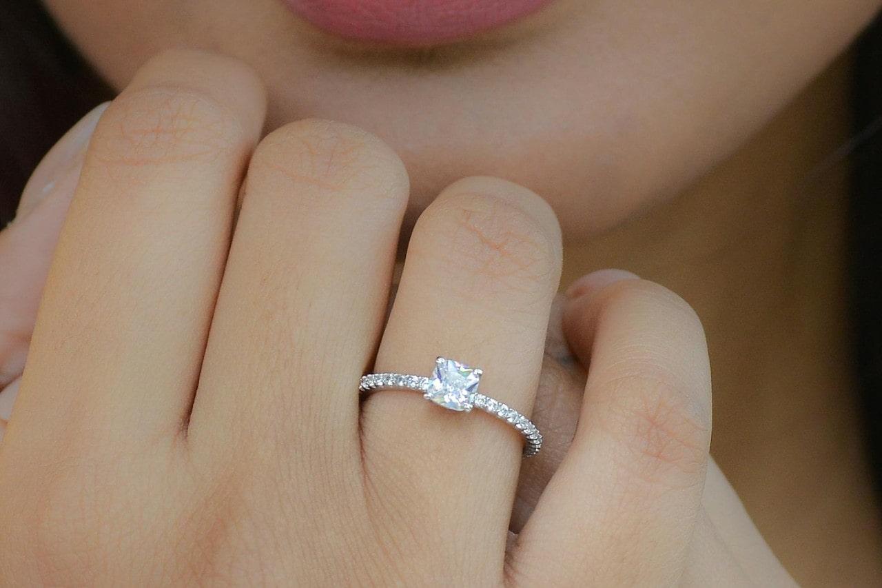 a woman’s hand held up to her chin, adorned with a cushion cut engagement ring
