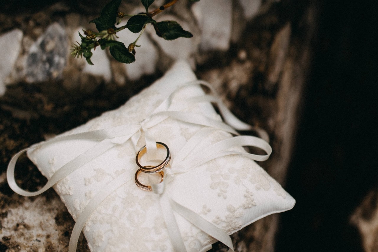 A pair of wedding rings sit on the ring bearer's pillow, secured with white ribbon.