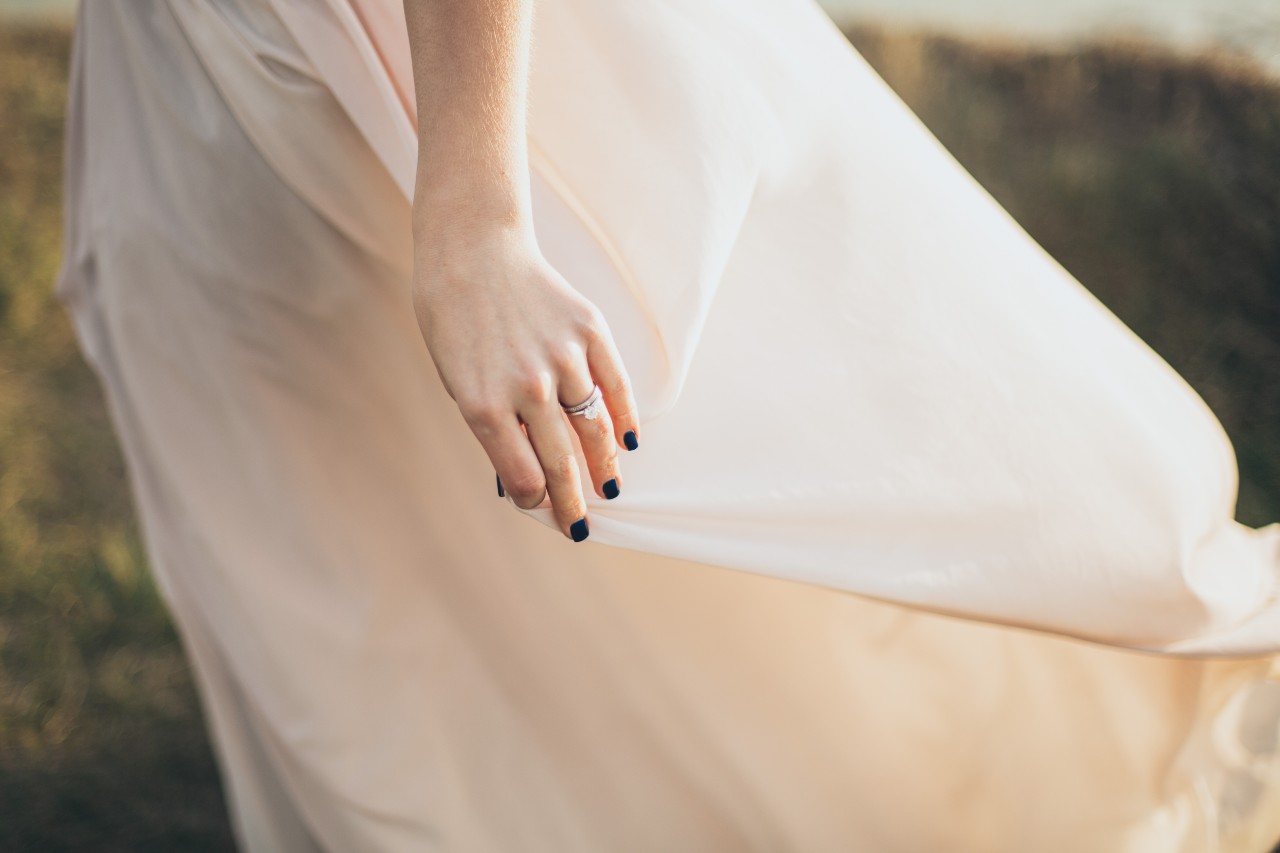 A bride with black manicured nails walks through a field, wearing her bridal jewelry.
