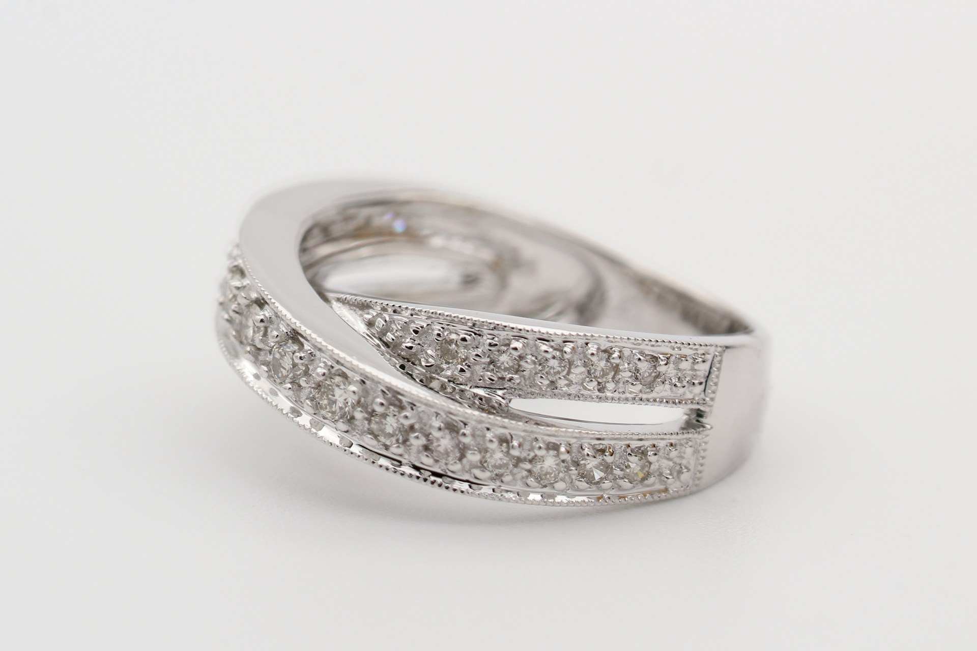 A detailed shot of a silver diamond-encrusted ring with an intricate, overlapping design, placed on a white surface.