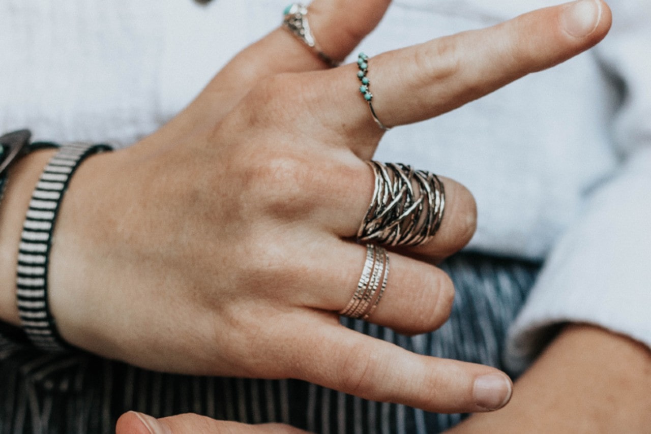 A close-up of a person's hand adorned with multiple silver rings, including a twisted band and a turquoise-stone ring.