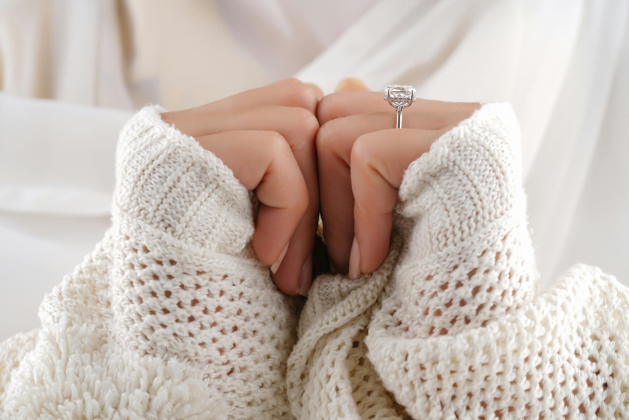 A close-up of a woman wearing a chunky knit sweater, with emphasis on her elegant engagement ring.