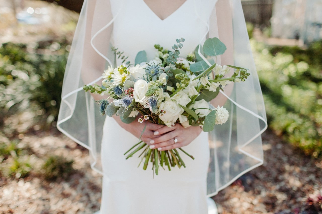 A close-up of a bride holding a delicate bouquet, her engagement ring visible on her hand.