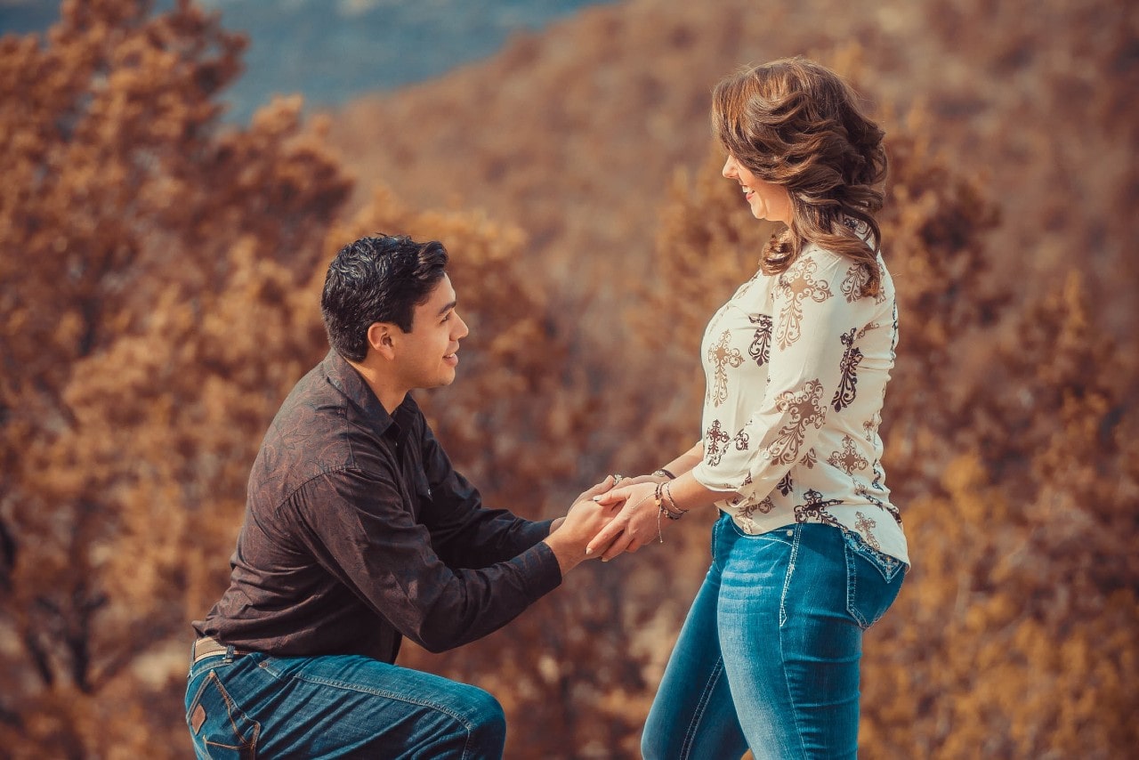 A man proposing to his partner among colorful autumn foliage.