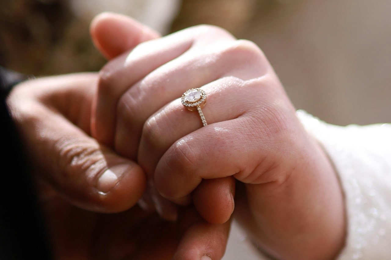 A close-up of a couple holding hands, with focus on the elegant engagement ring on her hand.