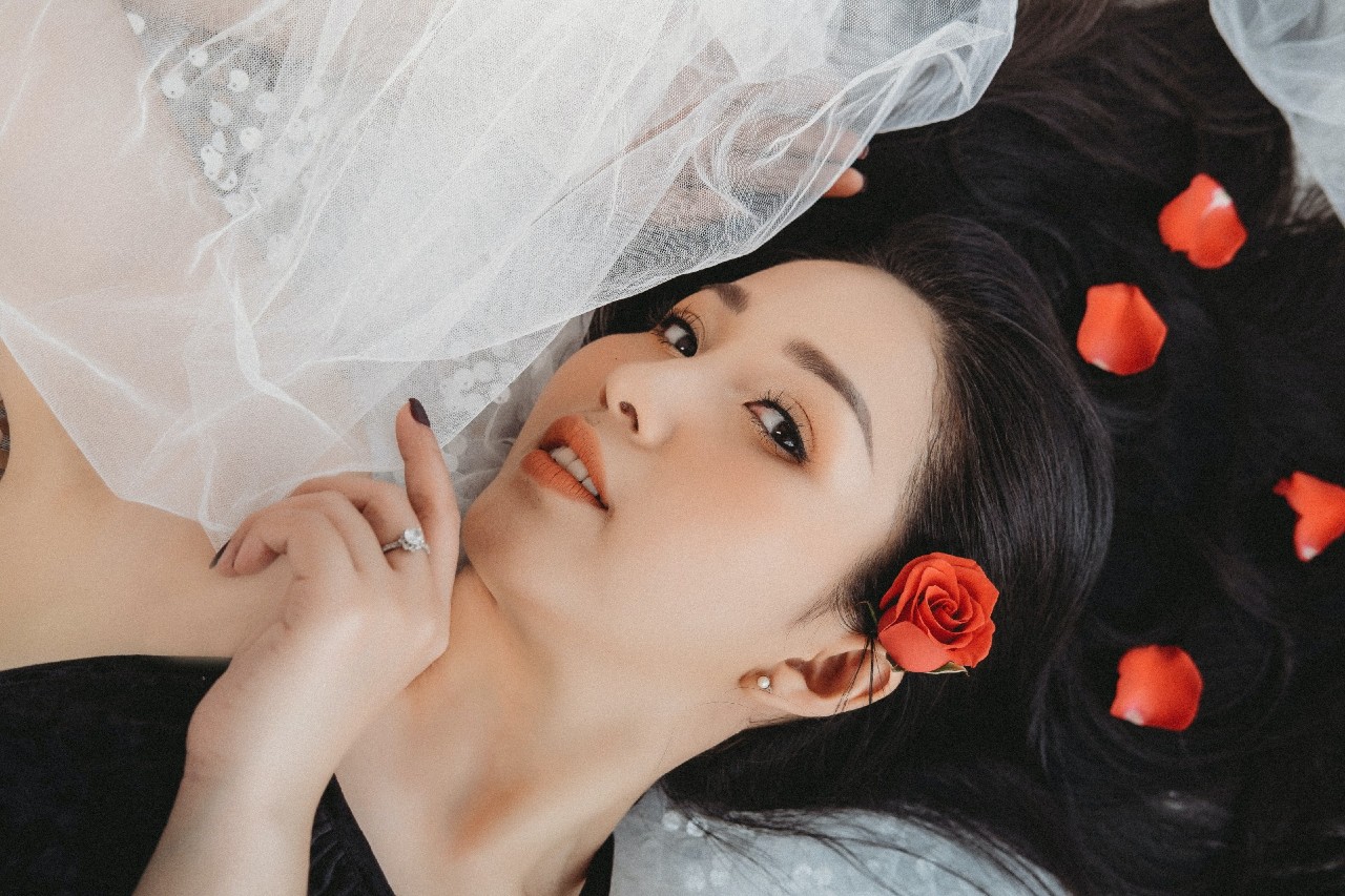 A close-up of a bride-to-be laying on her veil, roses in her hair and an engagement ring on her hand.