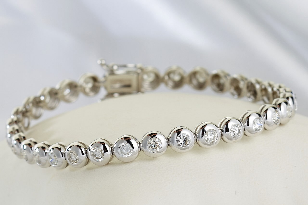 A close-up image of a white gold diamond bracelet with bezel set gems.