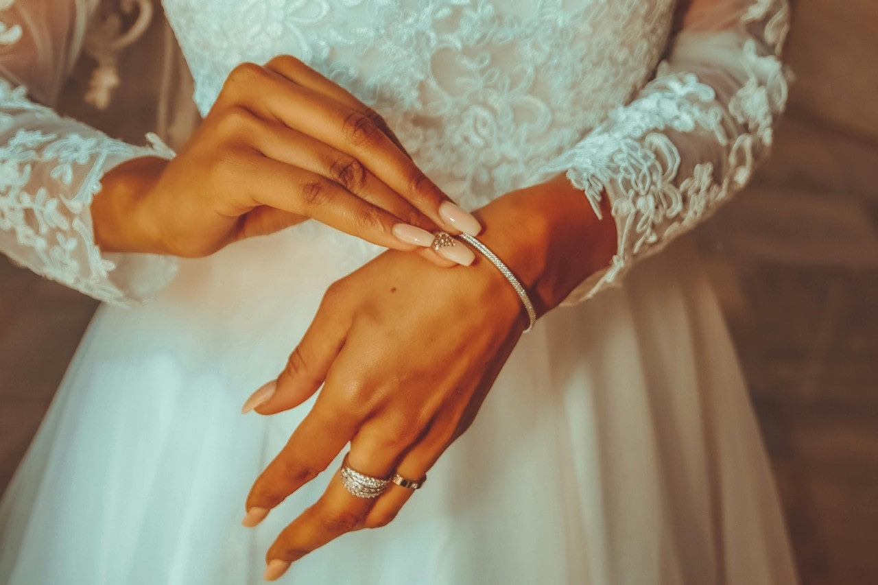 A close-up of a bride putting on a white gold diamond bangle bracelet.