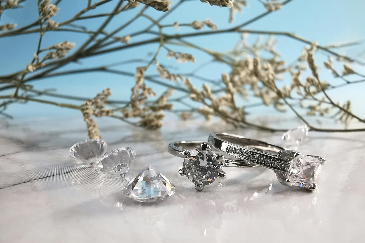 Two elegant diamond rings displayed alongside three round cut diamonds on a beachy backdrop.