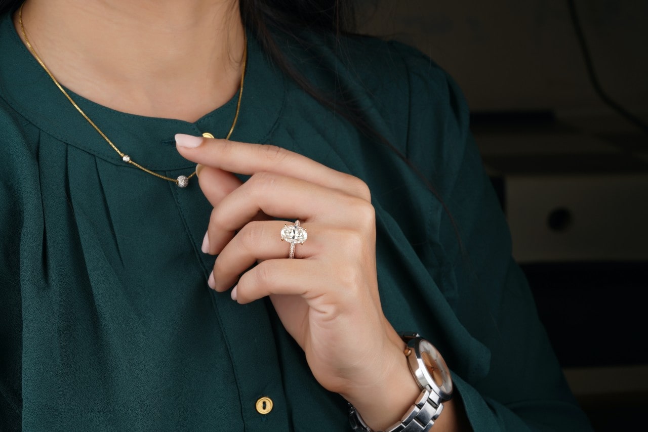 A close-up of a woman’s hand, wearing an oval cut engagement ring.