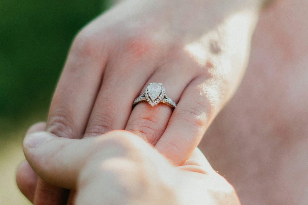 A close-up of a bride-to-be’s hand in her groom’s, her finger adorned with an elegant pear cut engagement ring.