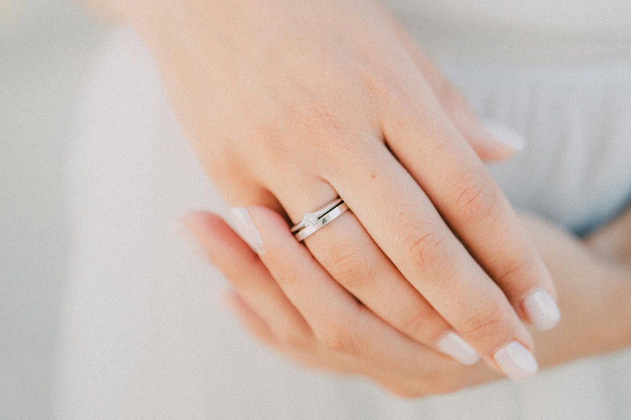 a woman’s hands, one of which is adorned with a white gold engagement ring and wedding band