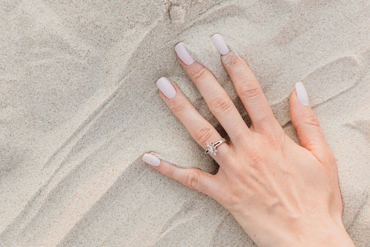 a woman’s hand in the sand, wearing a marquise cut engagement ring